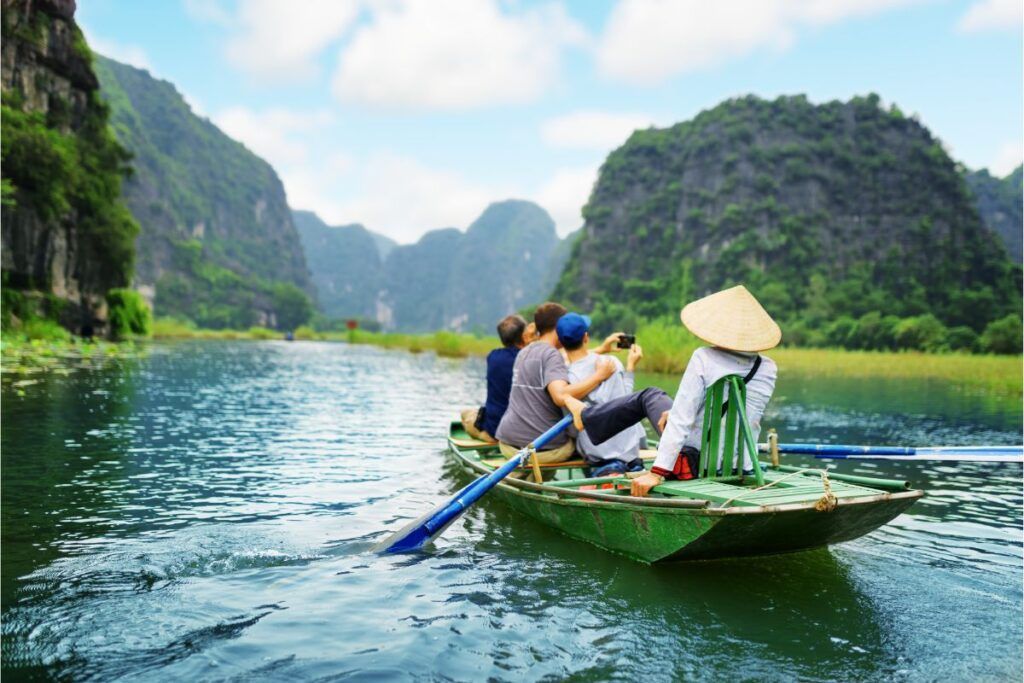 Vietnam: Touristen in einem Boot auf einem Fluss, umgeben von grünen Karstfelsen.