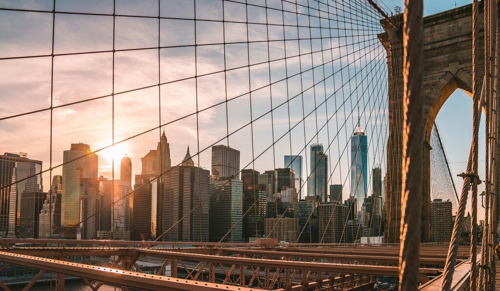 Die Sonne geht hinter der Skyline von New York City unter, gesehen durch die Kabel der Brooklyn Bridge.