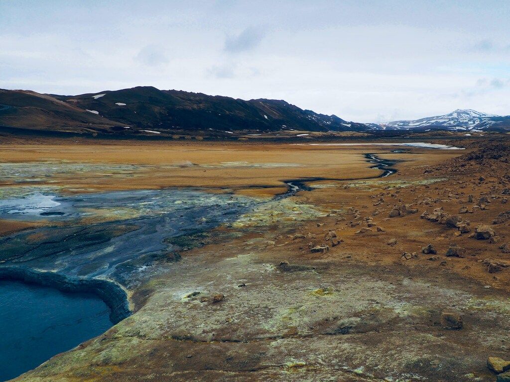 Weite, karge Landschaft mit Bergen im Hintergrund und einem kleinen Fluss, der sich durch das Gelände schlängelt.