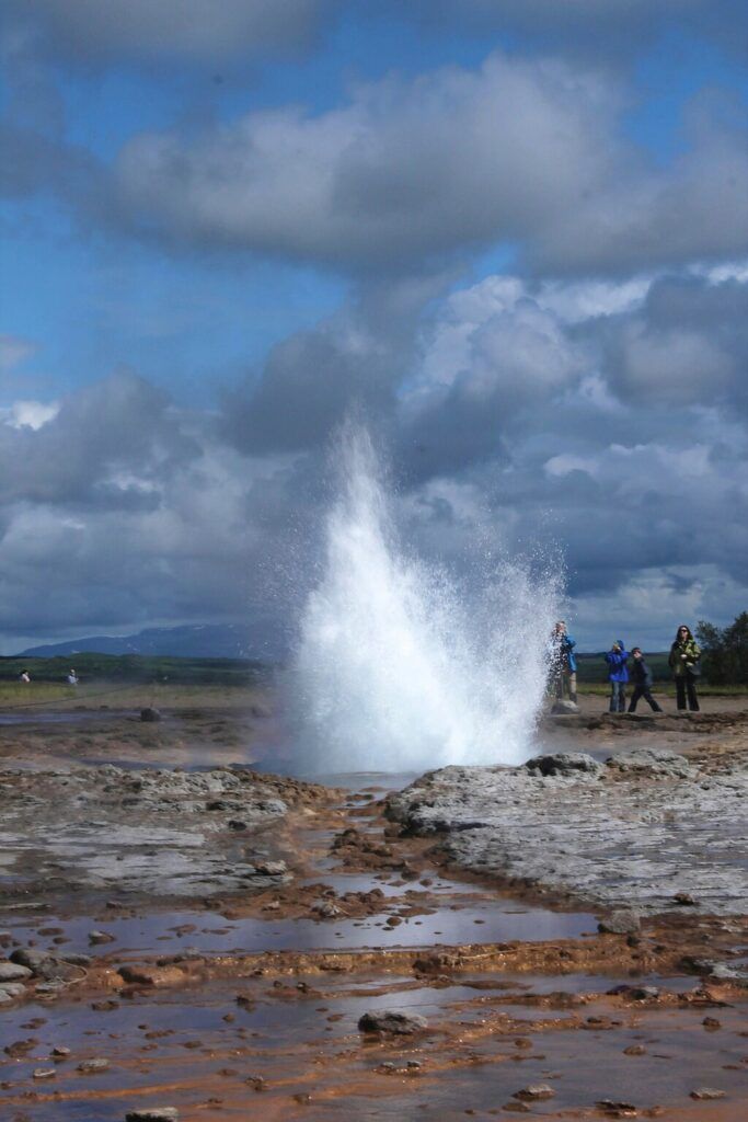 Heiße Quelle mit einem ausbrechenden Geysir vor klarem, blauem Himmel.