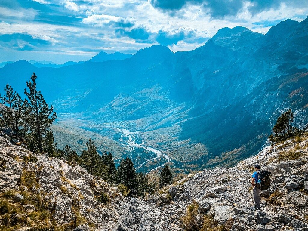 Wanderer auf felsigem Bergpfad mit Tal und Bergen im Hintergrund