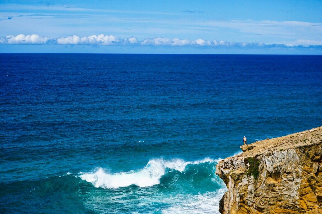 Person steht tagsüber auf einer Felsformation am Meer