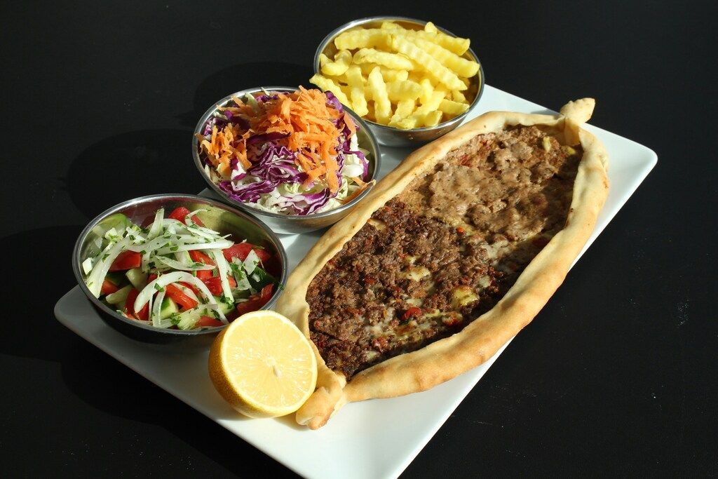 Ein weißer Teller mit einer mit Fleisch gefüllten Pastete neben Schüsseln mit Salat und Pommes