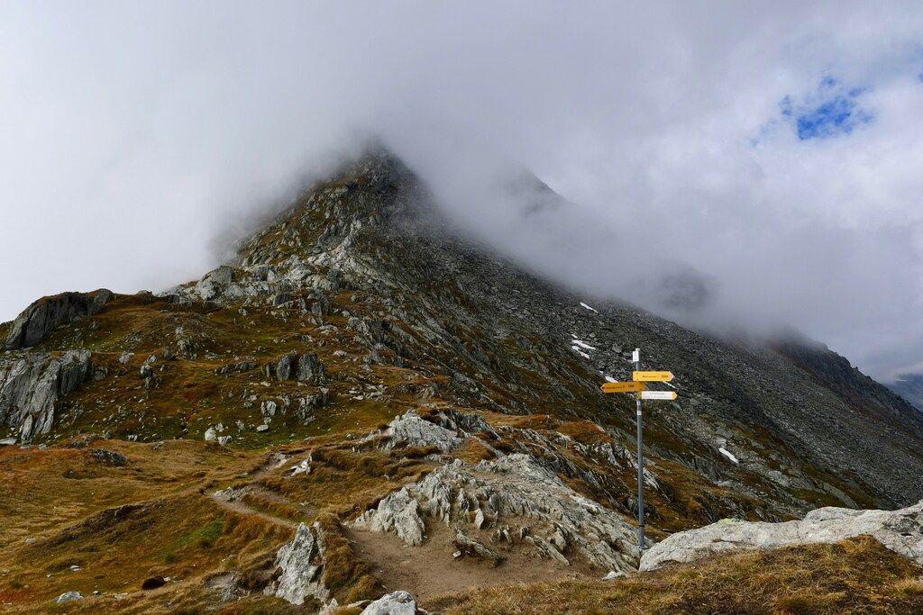 Berggipfel in Wolken gehüllt mit Wanderweg und Wegweisern im Vordergrund