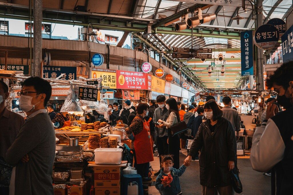 Belebter Markt mit Essensständen und maskierten Besuchern