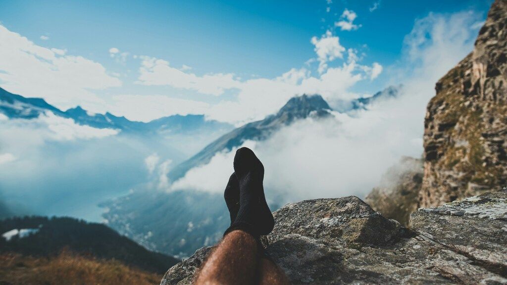 Ein Wanderer entspannt auf einem Felsen mit Blick auf nebelverhangene Berge und Täler