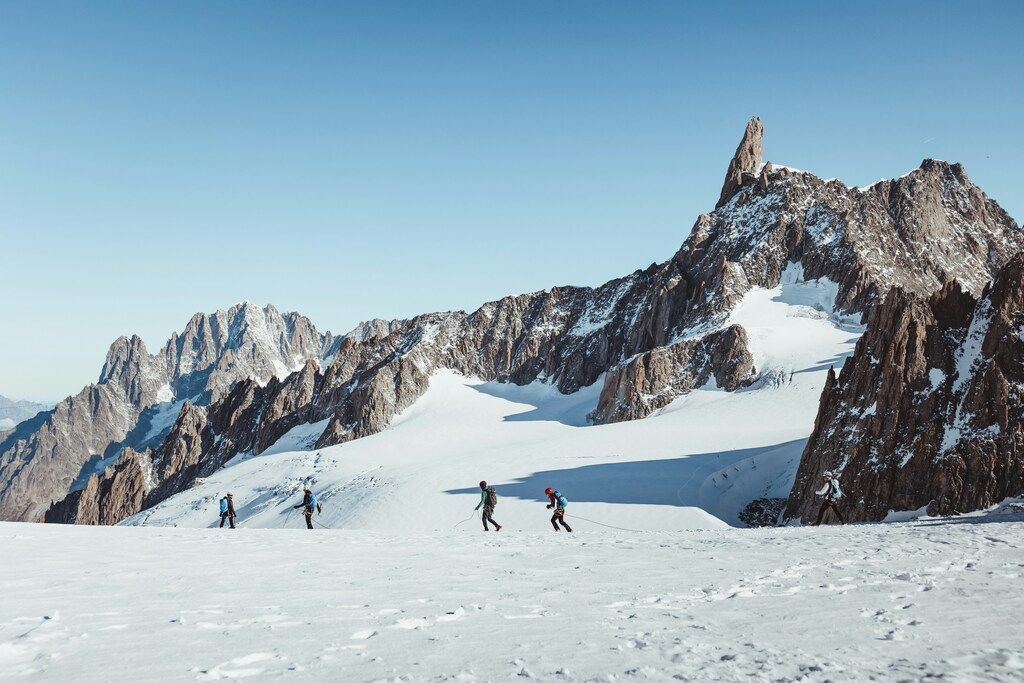 Bergsteiger überqueren ein schneebedecktes Hochplateau mit gezackten Gipfeln im Hintergrund: Alpenwanderung