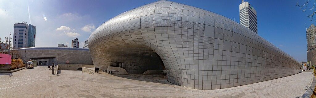 Ein futuristisches Gebäude mit geschwungenen, metallischen Oberflächen steht inmitten einer modernen Stadtlandschaft