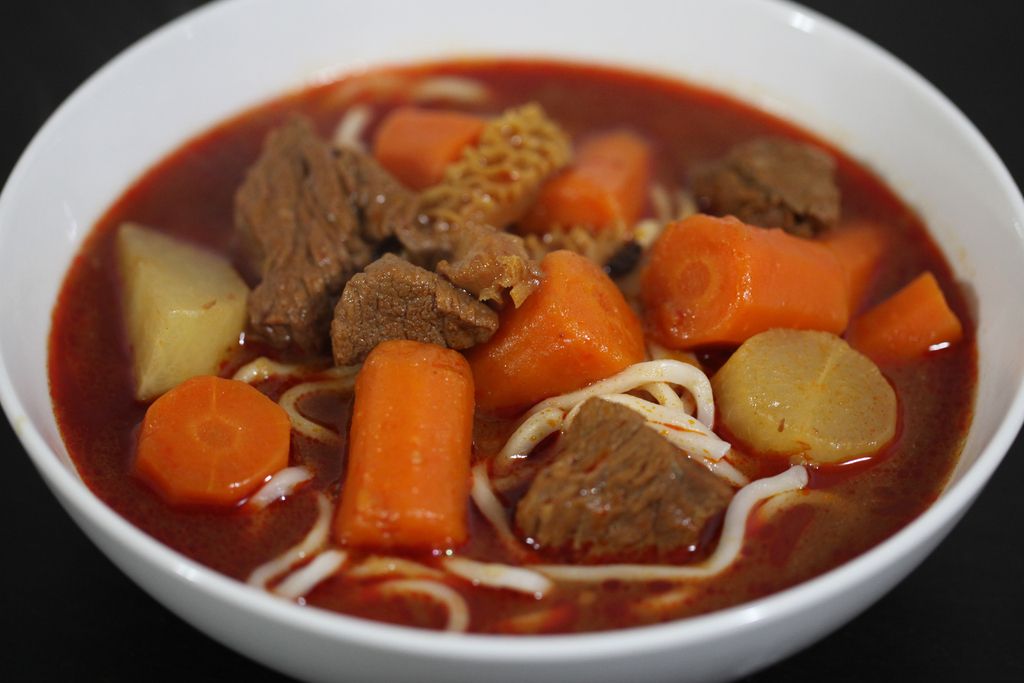 Vietnamesisches Essen: vietnamesischer Rindereintopf mit Karotten, Kartoffeln und Nudeln in einer roten Brühe.