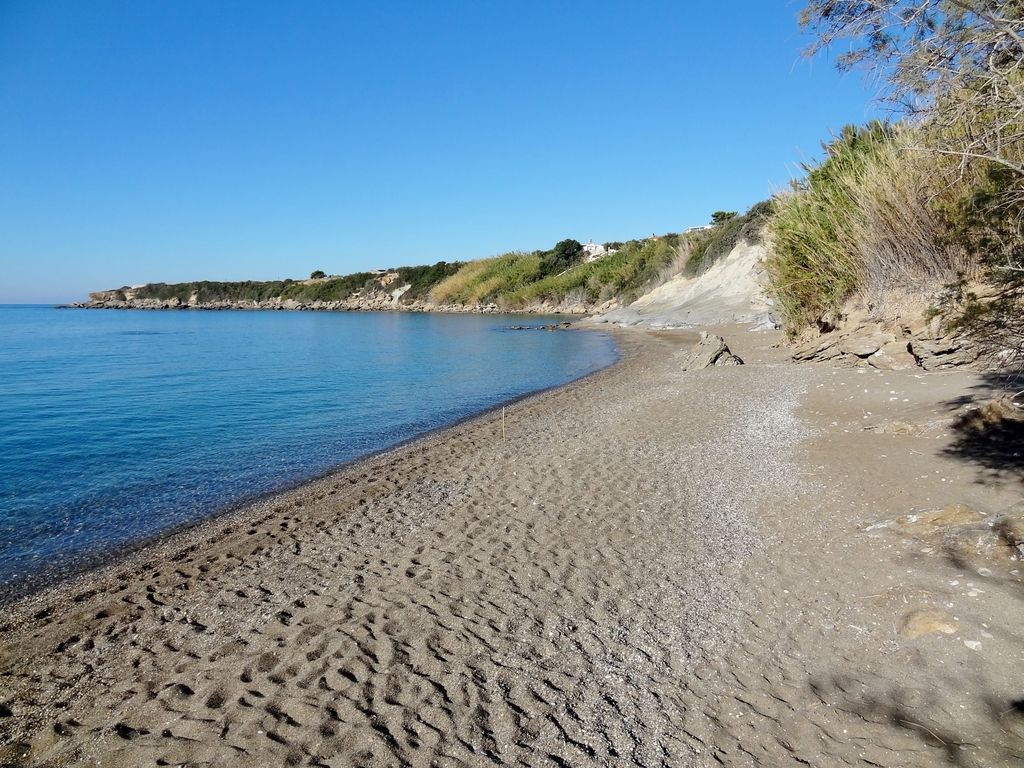 Albaniens Stränden: Ruhiger Sandstrand mit klarem Wasser an der Küste, umgeben von sanftem Grün und felsigen Klippen im Hintergrund.