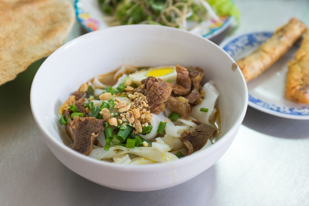 Vietnamesisches Essen: vietnamesische Nudeln mit Rindfleisch, Frühlingszwiebeln und Erdnüssen, serviert mit Beilagen wie Reispapier und Frühlingsrollen.