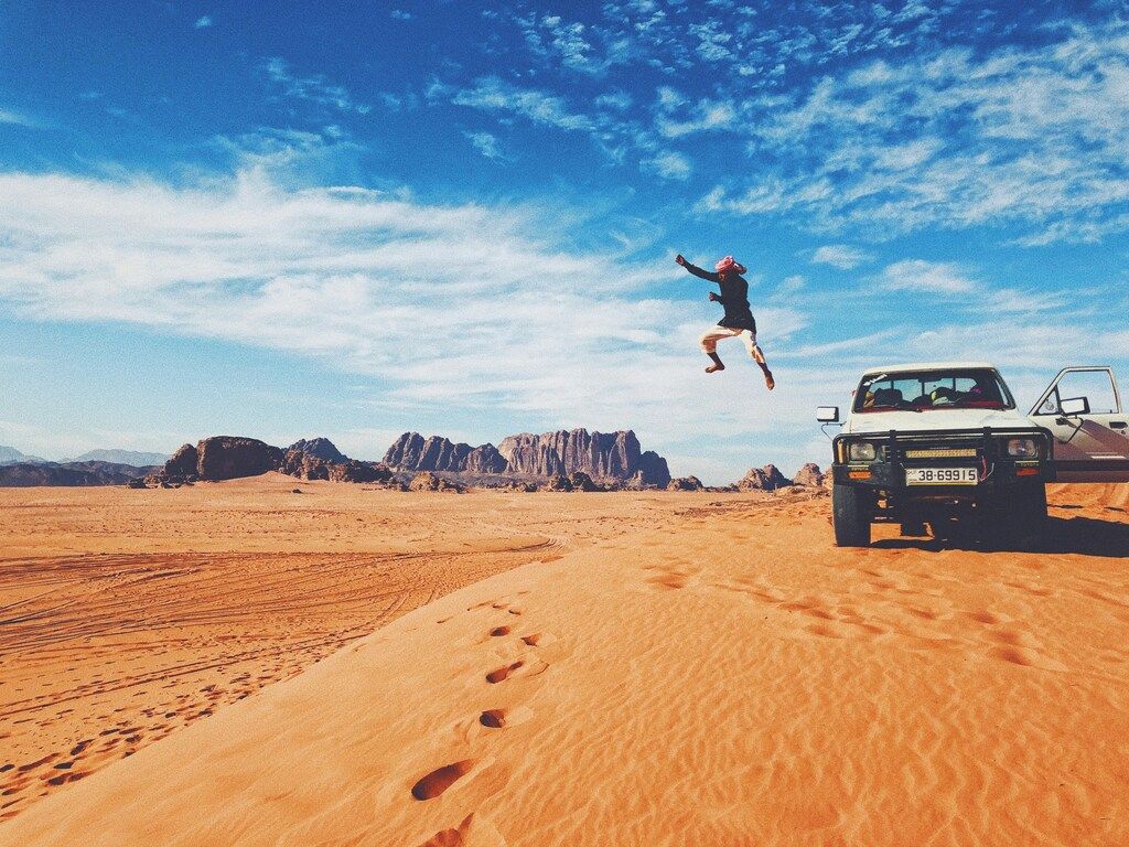 Petras Sehenswürdigkeiten: Person, die in der Wüste Wadi Rum neben einem Geländewagen springt