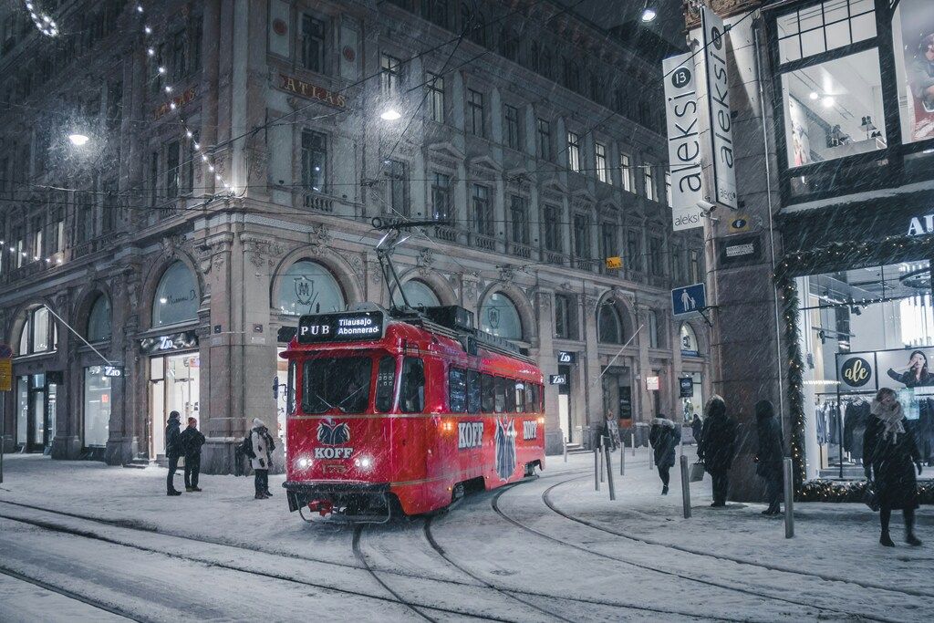 Eine rote Straßenbahn fährt durch eine verschneite Straße im Zentrum von Helsinki, beleuchtet von Stadtlichtern