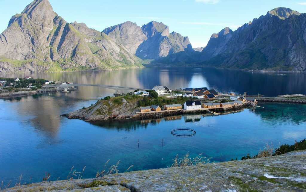 Ein kleines Dorf mit traditionellen Holzhäusern, umgeben von tiefblauem Wasser und majestätischen Bergen.