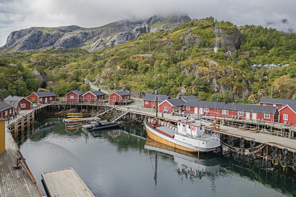 Ein kleiner Hafen mit roten Fischerhütten, Booten und grüner Berglandschaft im Hintergrund