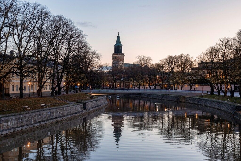 Blick auf den Dom von Turku bei Dämmerung, mit Bäumen und einem ruhigen Fluss.