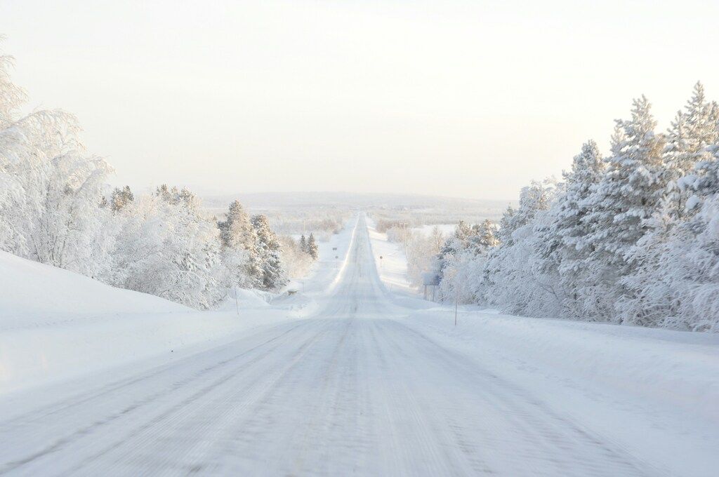 Eine lange, einsame Straße, bedeckt mit Schnee, umgeben von schneebedeckten Bäumen in einer stillen Winterlandschaft.