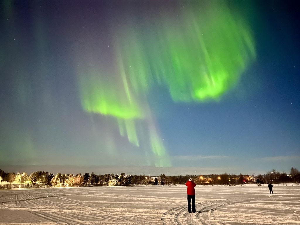 Person beobachtet grüne Nordlichter über einer verschneiten Landschaft.