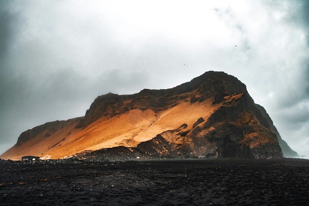 Brauner Berg in der Nähe eines Gewässers bei bewölktem Himmel am Tag