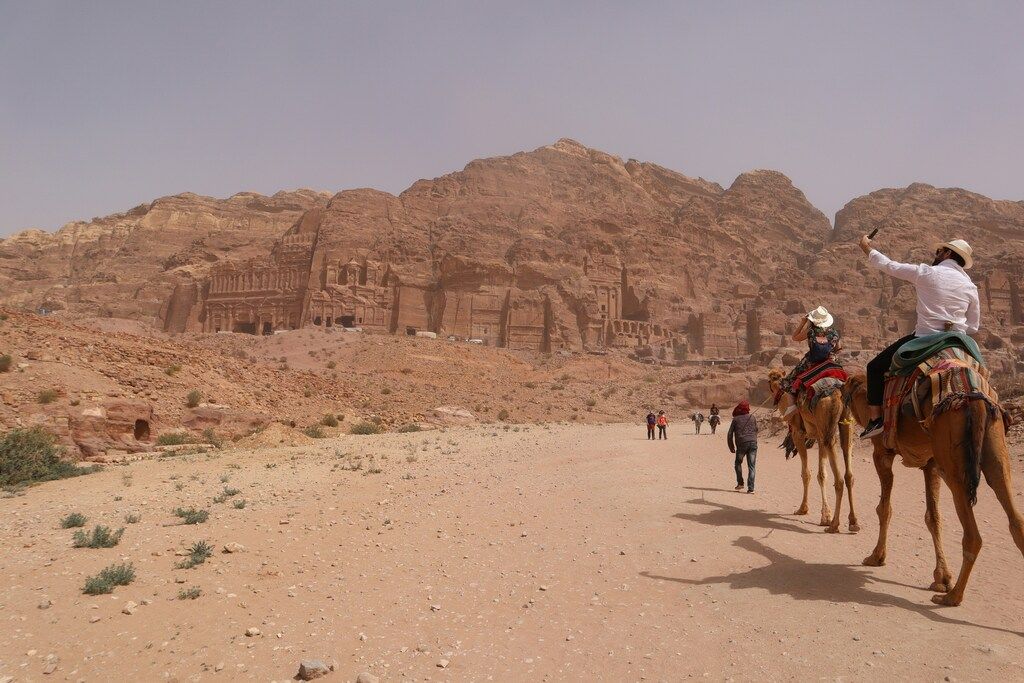 Touristen auf Kamelen vor Felsfassaden in Petra