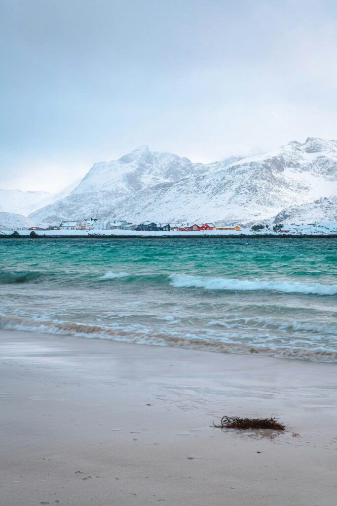 Ein schneebedecktes Bergpanorama hinter einem türkisblauen Meer, das sanft an den weißen Sandstrand rollt.