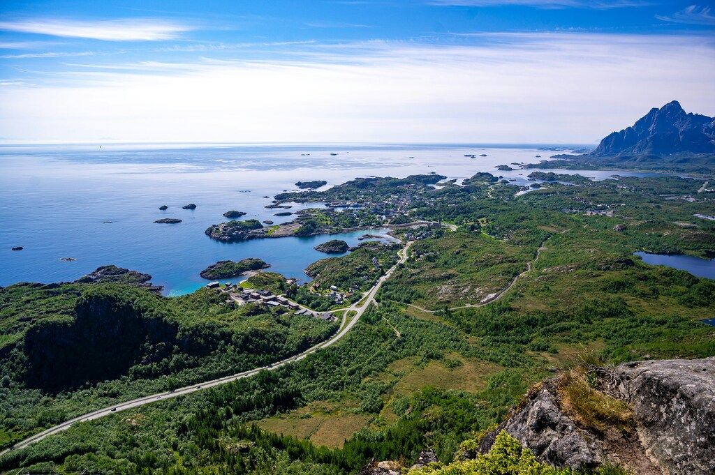 Lofoten Sehenswürdigkeiten: Ein atemberaubender Blick auf eine Küstenlandschaft mit grünen Hügeln, kleinen Inseln und weitläufigem Meer unter klarem Himmel.