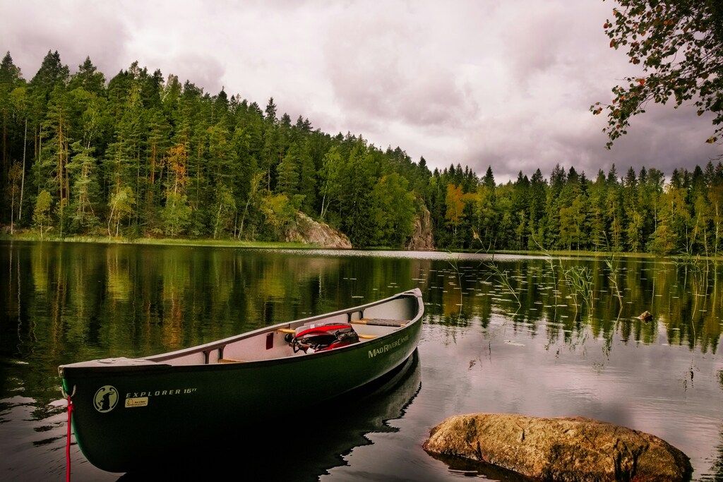 Ein grünes Kanu auf einem ruhigen See, umgeben von Bäumen in einem finnischen Wald.