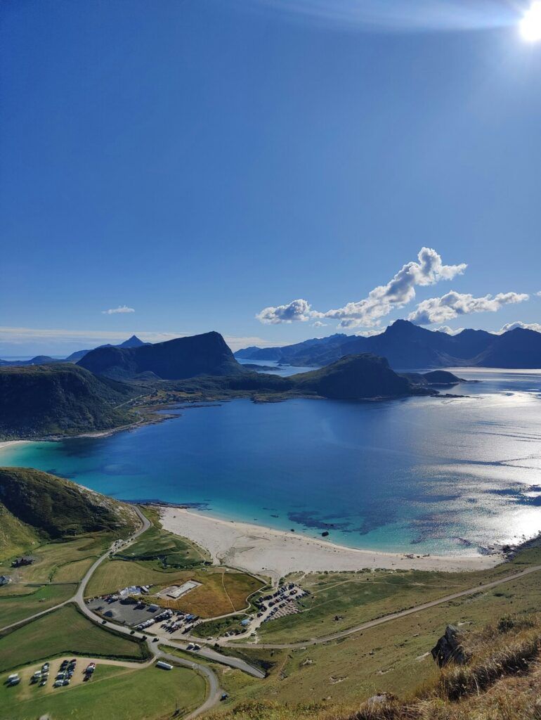 Ein weißer Sandstrand mit türkisblauem Wasser, umgeben von grünen Hügeln und Bergen unter strahlend blauem Himmel