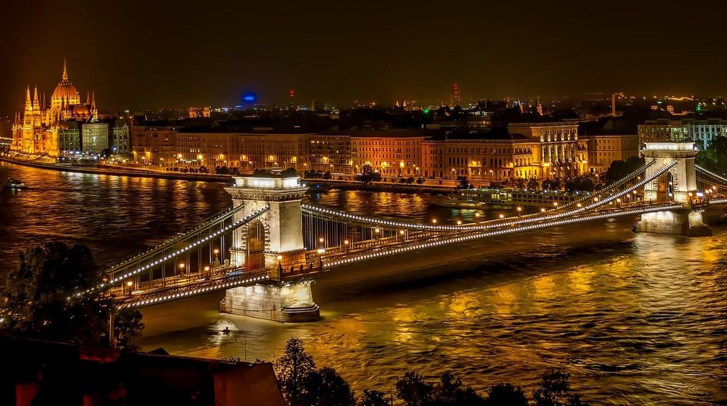 Die beleuchtete Kettenbrücke in Budapest bei Nacht mit dem Parlamentsgebäude im Hintergrund.