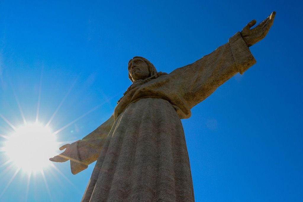 Cristo Rei Statue in Lissabon mit ausgebreiteten Armen und der Sonne im Hintergrund, ein ikonisches Denkmal.