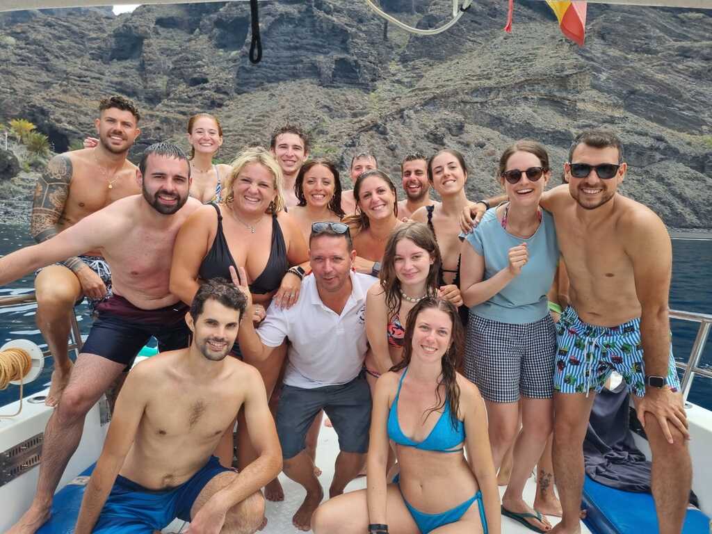 Gruppenfoto während einer organisierten WeRoad-Reise auf Teneriffa, aufgenommen auf einem Boot mit beeindruckenden Klippen im Hintergrund.