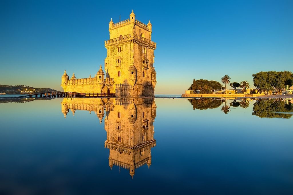 Der Torre de Belém in Lissabon, der sich im ruhigen Wasser spiegelt, bei goldenem Sonnenuntergang.