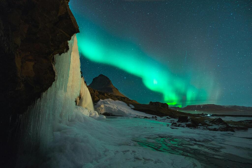 Faszinierende Nordlichter über einer eisigen Landschaft und einem Wasserfall in Island.
