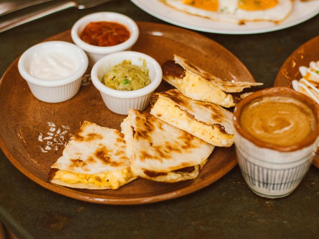 Quesadillas mit Guacamole, Sauerrahm und Salsasoße auf einem Teller.