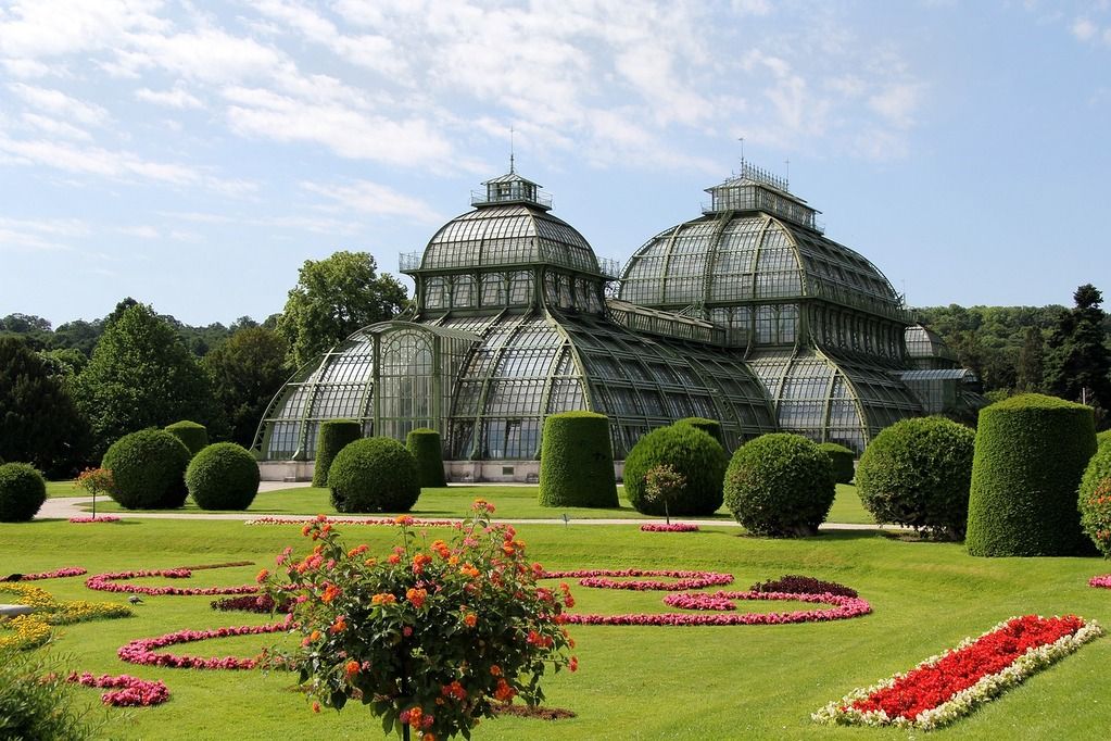 Das prachtvolle Palmenhaus im Schloss Schönbrunn in Wien umgeben von bunten Gärten.