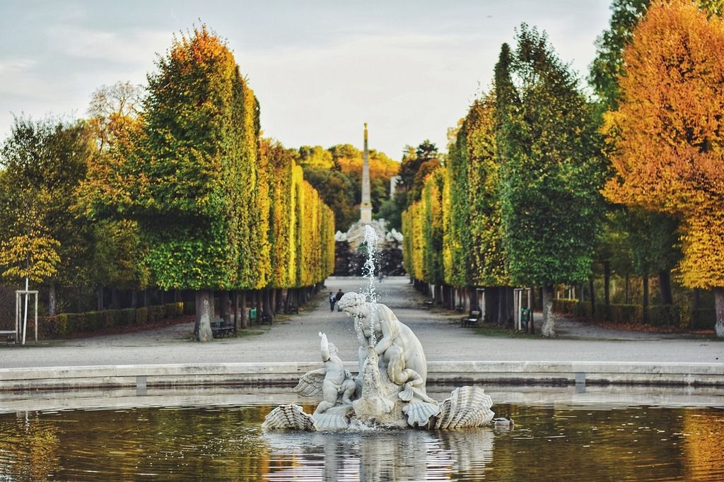 Ein malerischer Herbstblick im Schlosspark Schönbrunn mit Bäumen und einem Brunnen.