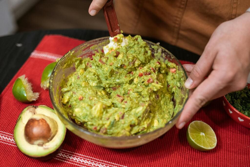 Frisch zubereitete Guacamole mit Limetten und Avocados auf einem roten Küchentuch.