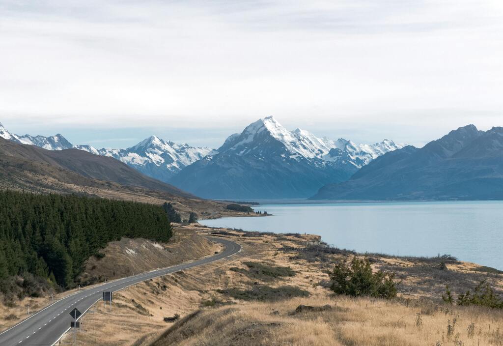 Malerische Straße, die entlang eines Sees in Richtung der schneebedeckten Berge von Neuseeland führt.