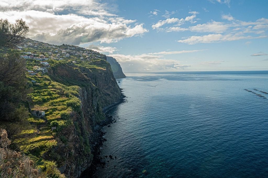 Steile Küstenklippen mit kleinen Häusern und grünen Terrassen auf Madeira.