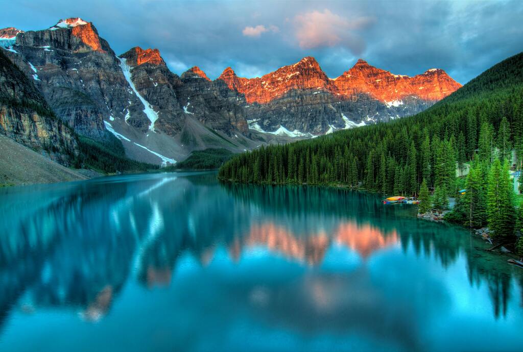 Moraine Lake im Banff-Nationalpark, umgeben von Bergen, die vom Sonnenuntergang beleuchtet werden.
