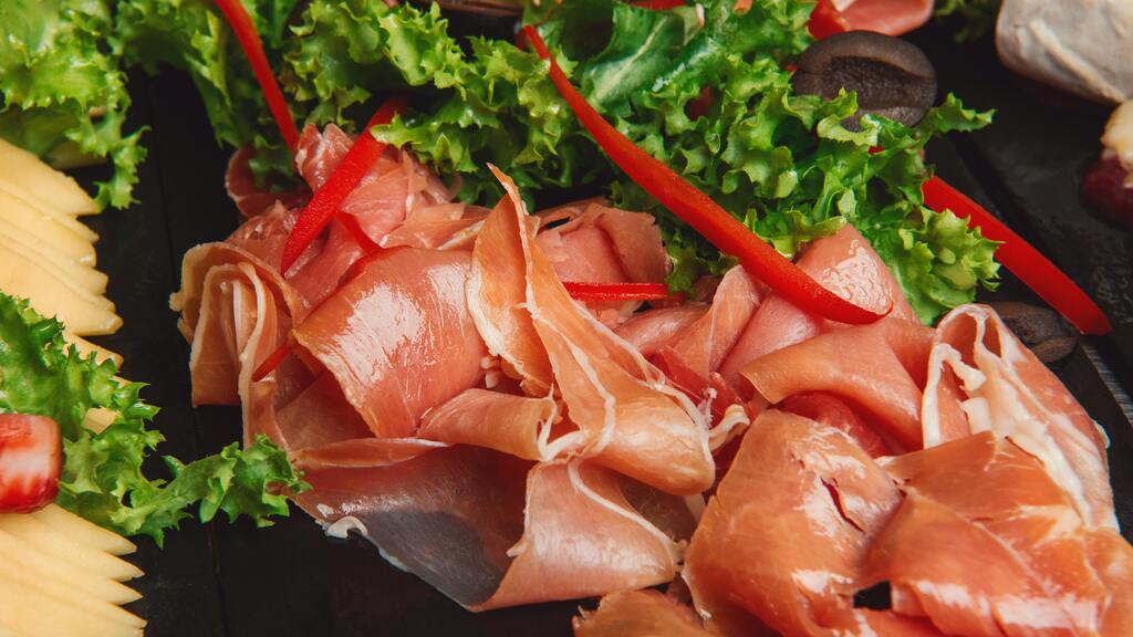 Italienische Schinken- und Käsespezialitäten mit frischem Salat und roten Paprikastreifen.