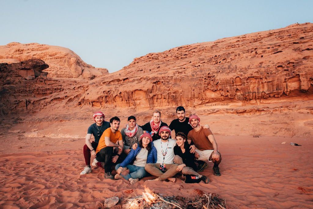 WeRoad Gruppe sitzt im roten Wüstensand von Jordanien rund um ein Lagerfeuer