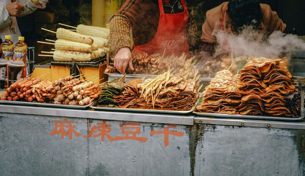 Straßenimbiss mit verschiedenen chinesischen Spießen und dampfendem Tofu.