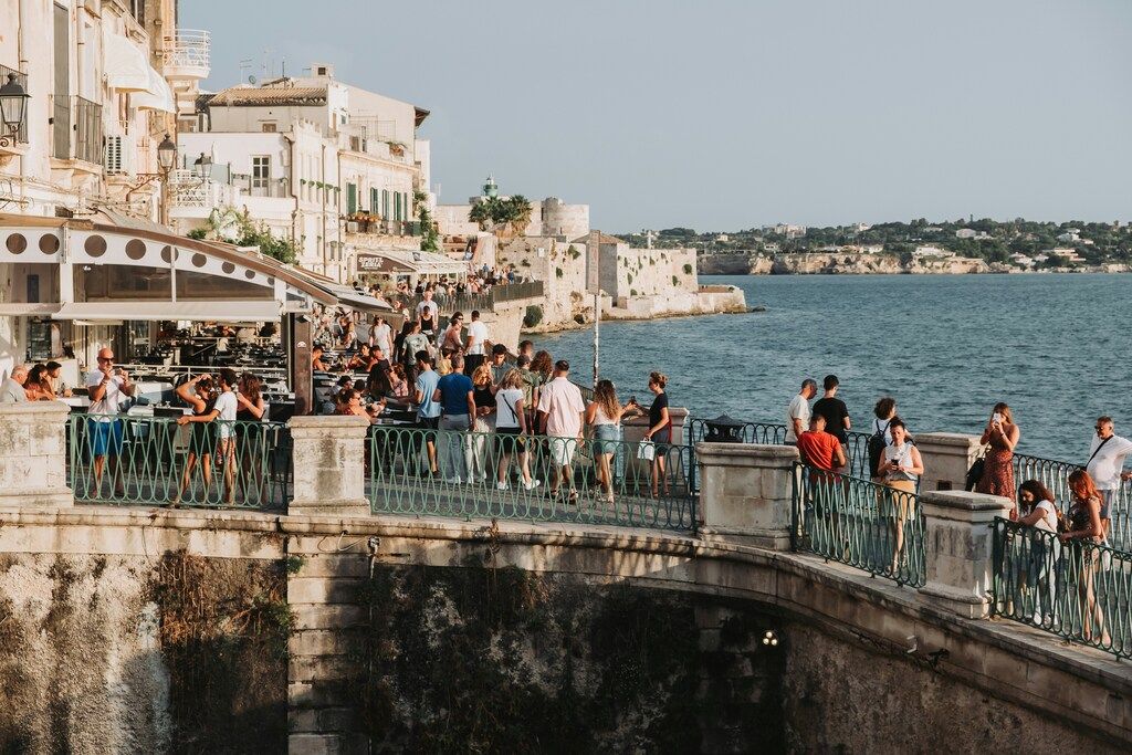 Menschen flanieren entlang der belebten Meerespromenade von Ortigia in Syrakus, Sizilien