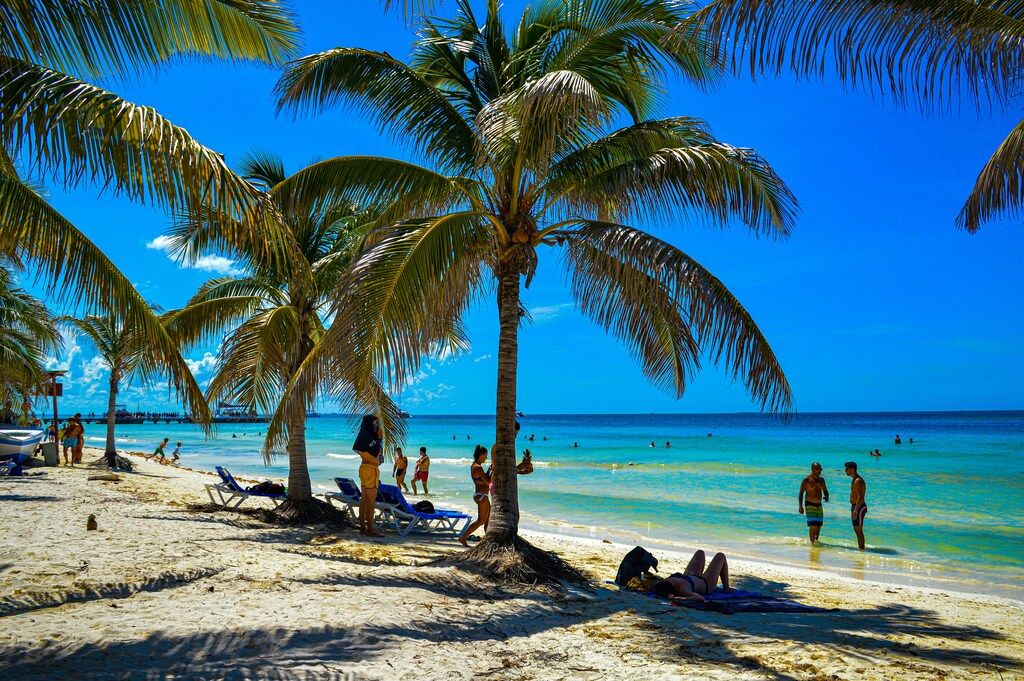 Tropischer Sandstrand mit Palmen und Badenden bei klarem, blauem Meer