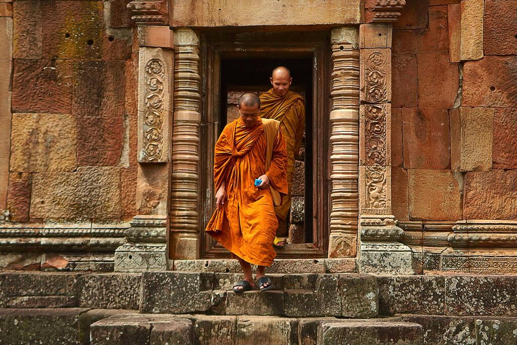 Zwei buddhistische Mönche in orangefarbener Robe verlassen einen alten Tempel in Thailand.
