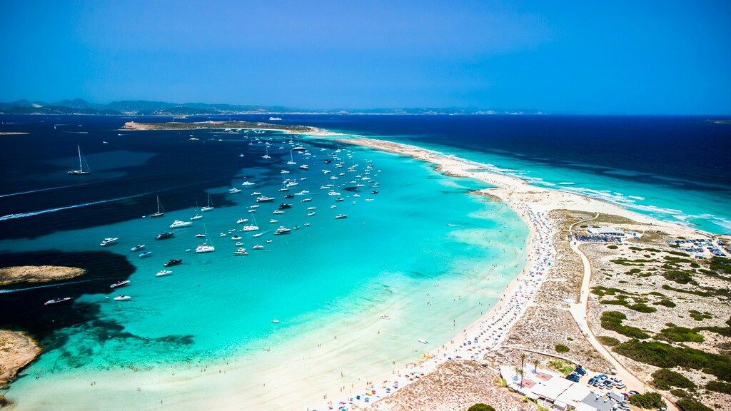 Luftbild der Playa de Ses Illetes auf Formentera mit vielen Booten und türkisfarbenem Wasser.
