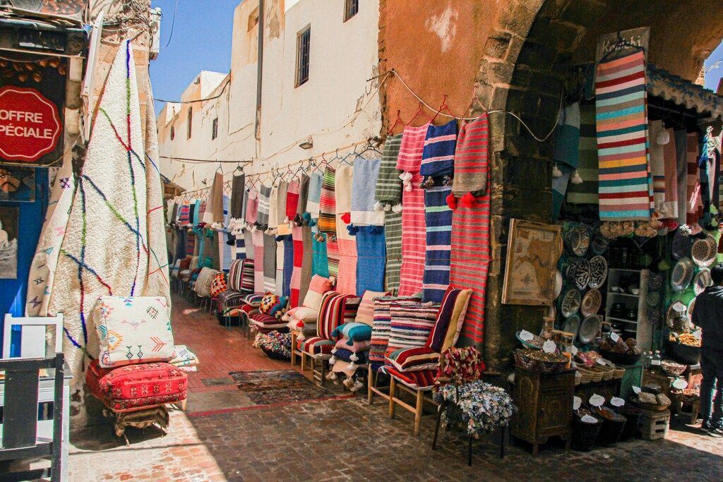 Farbenfroher Souk in Marokko mit Teppichen, Kissen und traditionellen Waren entlang der Gassen