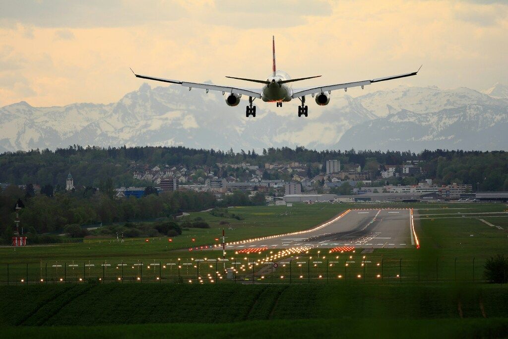 Flugzeug im Landeanflug auf eine beleuchtete Landebahn mit Bergen im Hintergrund.