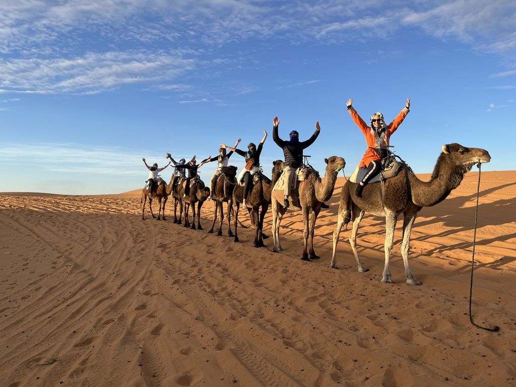 Touristengruppe reitet auf Kamelen durch die Sanddünen der marokkanischen Wüste.